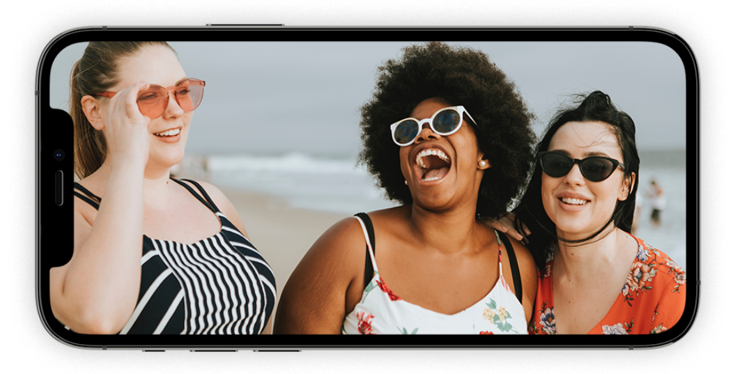 Three women wearing sunglasses and laughing on the beach.