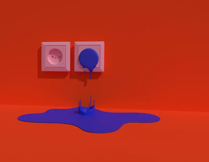 A blue liquid appears to spill from a wall socket onto an orange floor, pooling beneath two white electrical outlets on a bright orange wall.