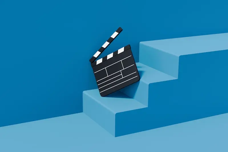 A black and white film clapperboard rests against the edge of blue steps against a blue background.