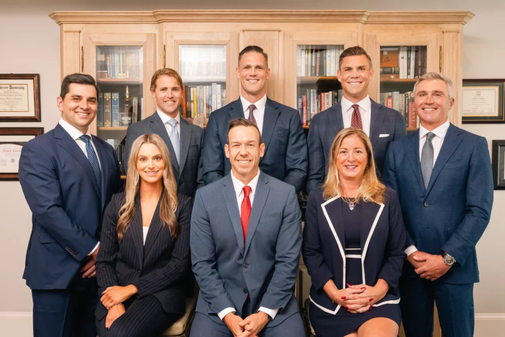 Eight professionally dressed people pose in two rows in an office setting with bookshelves and diplomas in the background.