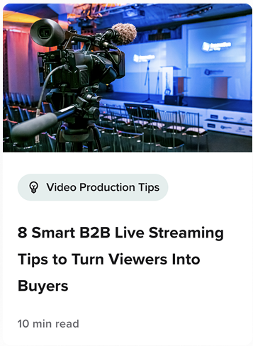 A professional video camera is set up in an empty event venue with rows of chairs and a stage prepared for a live-streamed presentation.