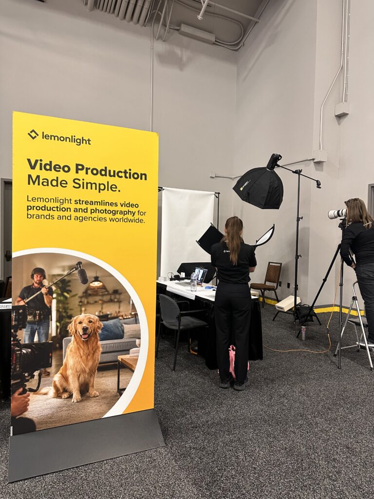 A Lemonlight booth features a large yellow banner about video production, with staff setting up photographic equipment and a photographer taking pictures in a studio area.