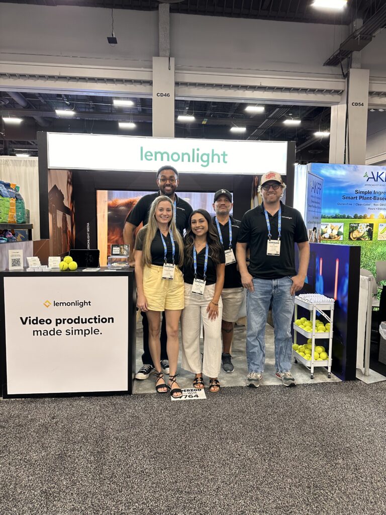 Four people stand in front of a Lemonlight booth at a convention, with a sign that reads, “Video production made simple.”.