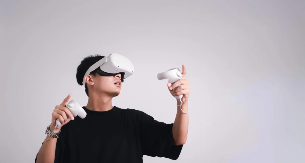 Person wearing a virtual reality headset, holding controllers, facing left against a plain background.